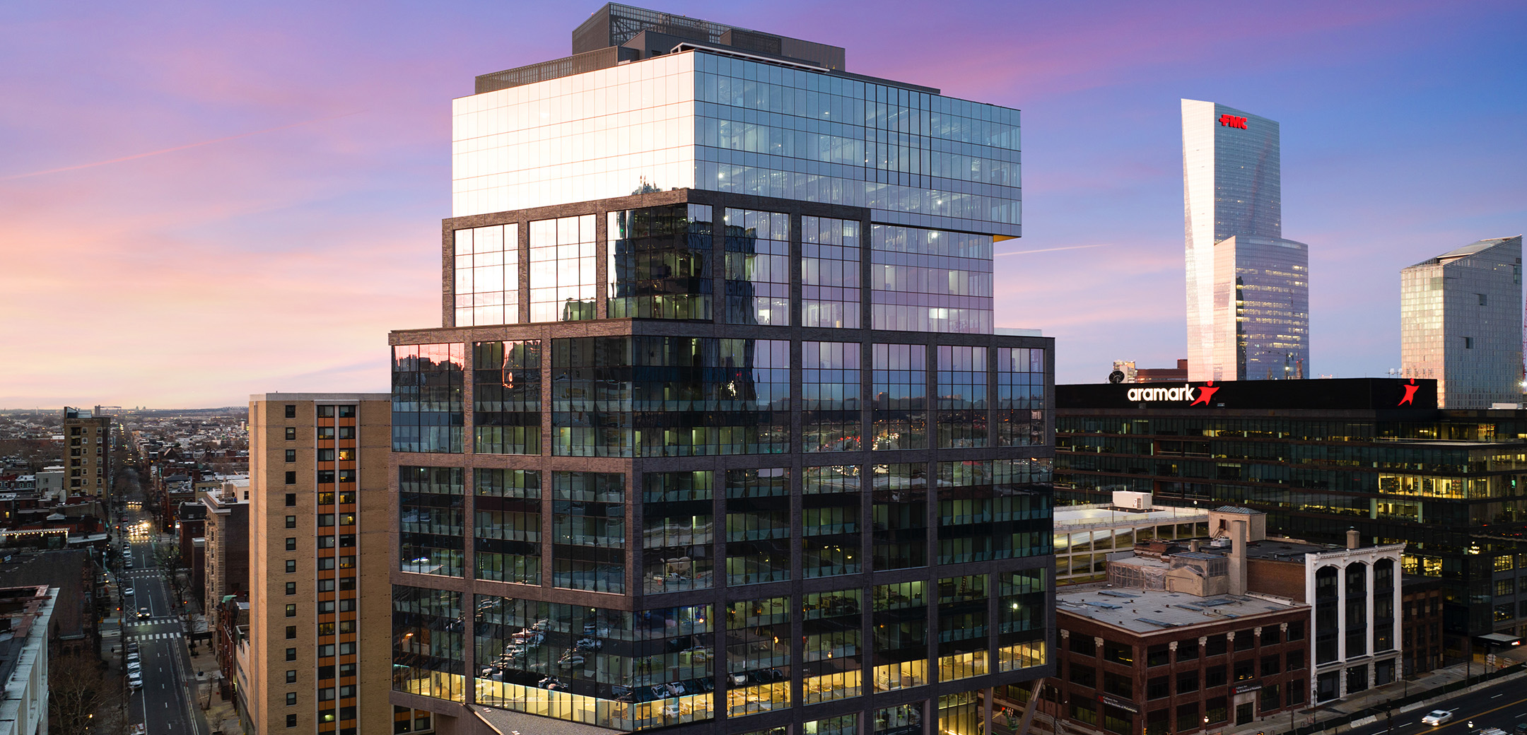 The exterior view of 2222 Market Street featuring a glass facade and the city of Philadelphia in the background