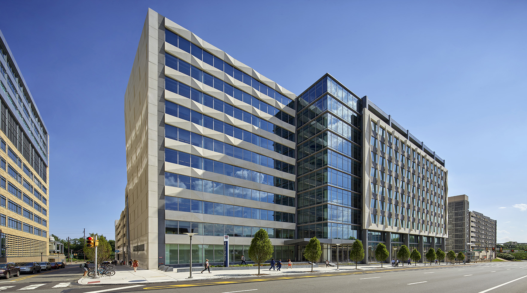 The exterior of a 10-story office tower for Penn Medicine featuring precast panels framing floor-to-ceiling glass on a street lined with trees in Philadelphia.