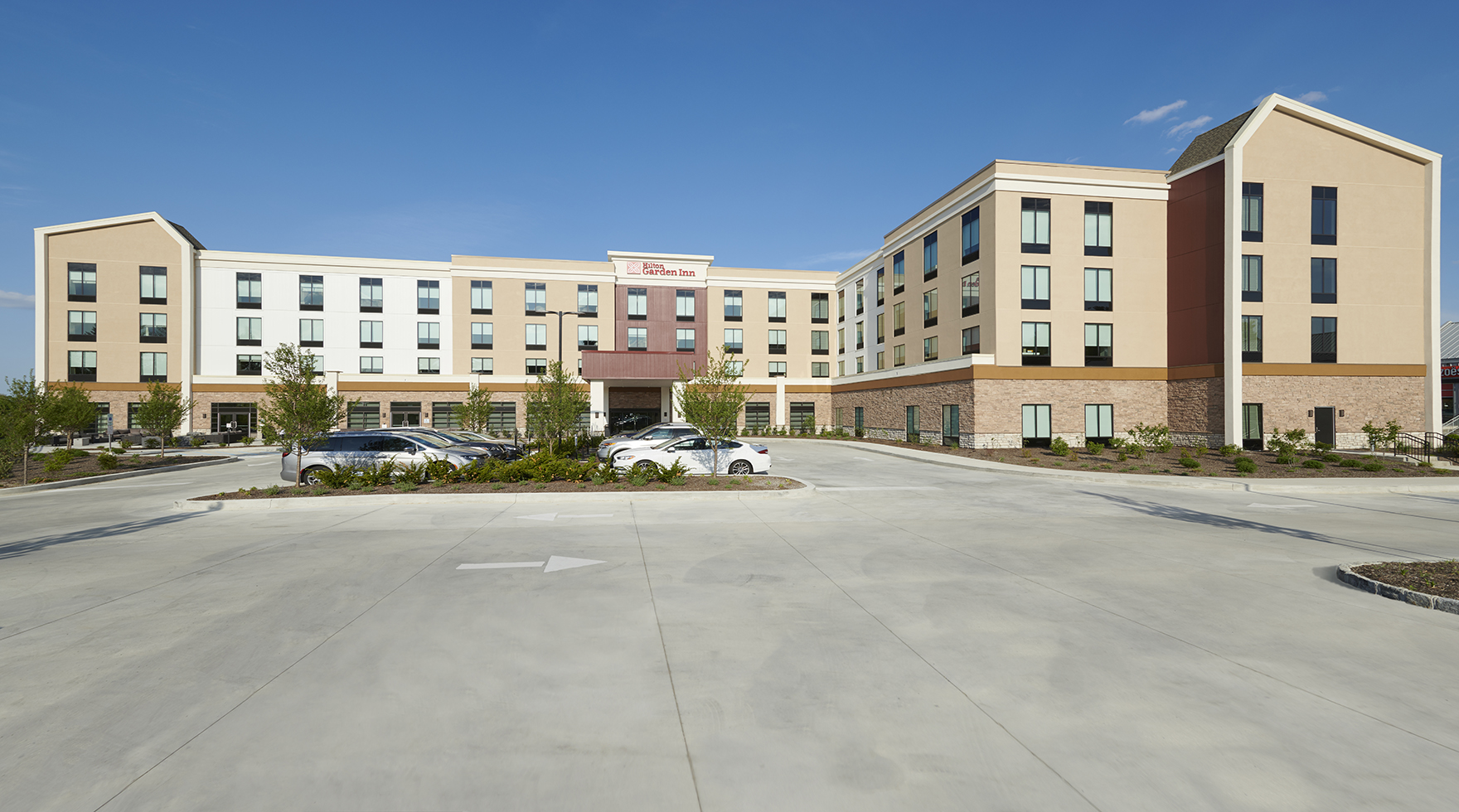 The exterior of the Hilton Garden Inn with a parking lot with cars in front.