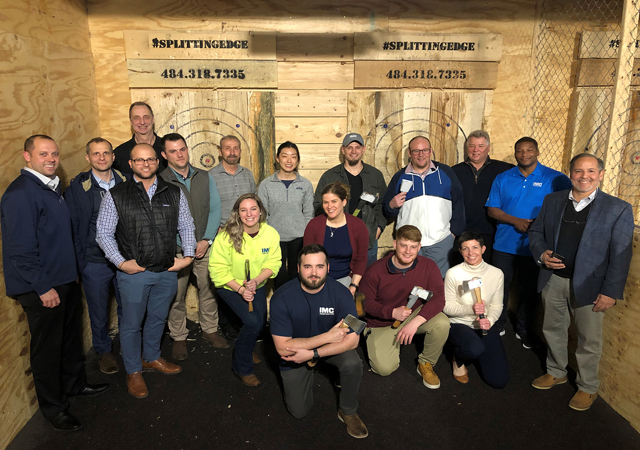 A group photo of IMC employees posing in front of a wood wall holding axes