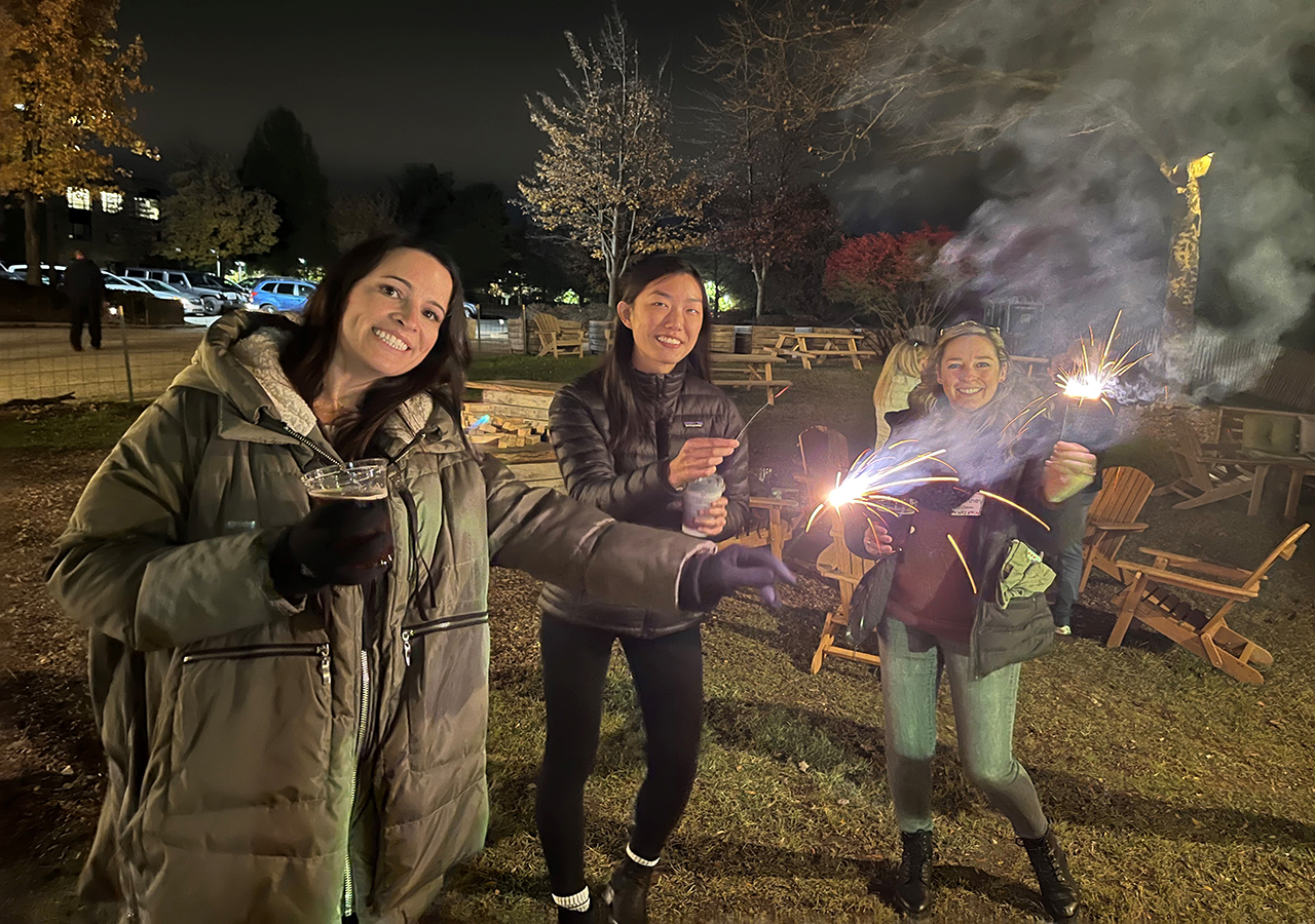 Three IMC employees holding sparklers and smiling outside in the dark.