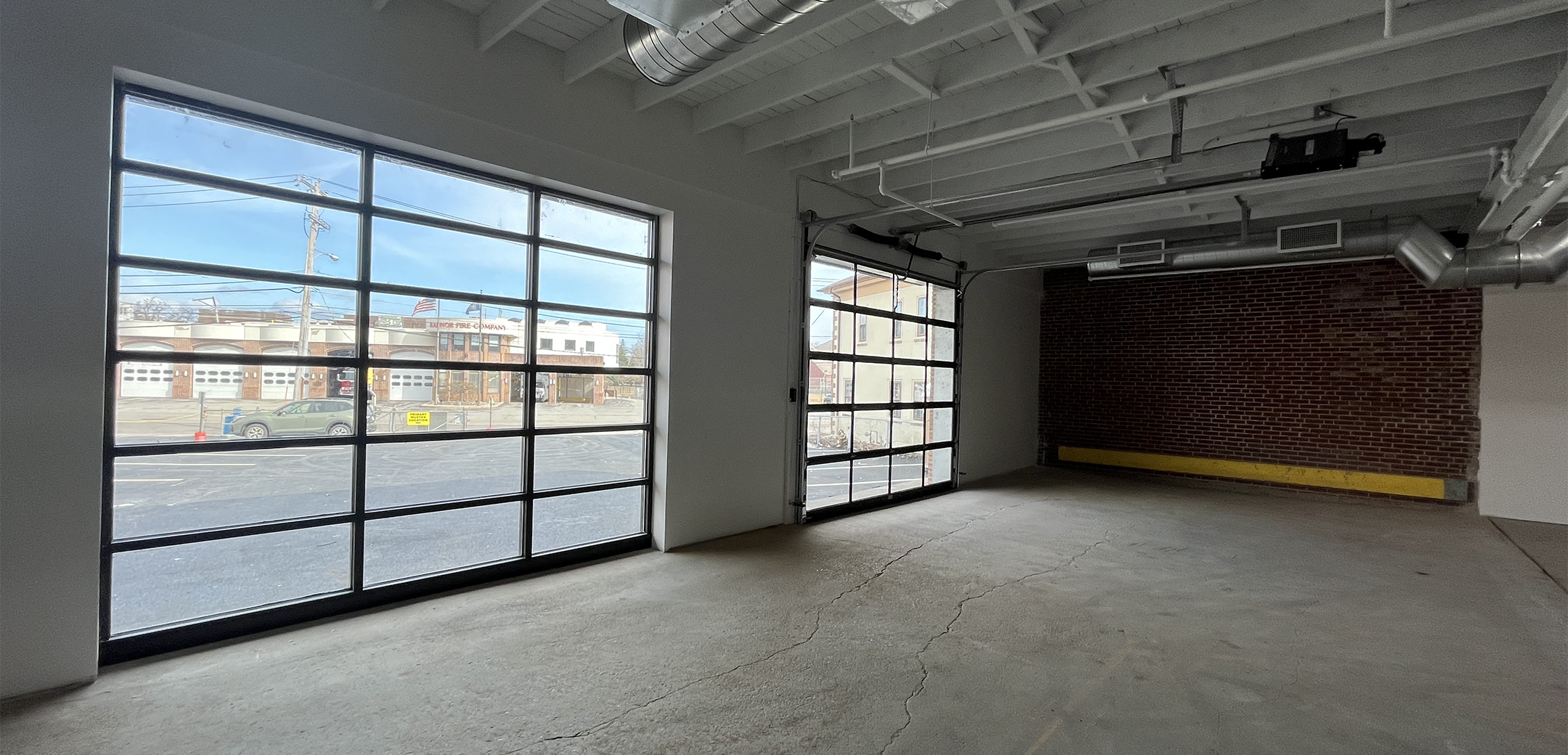 An angled interior view of the 108 Wayne Ave glass garage shutter doors looking outside, industrial vents on the ceiling and back brick wall.