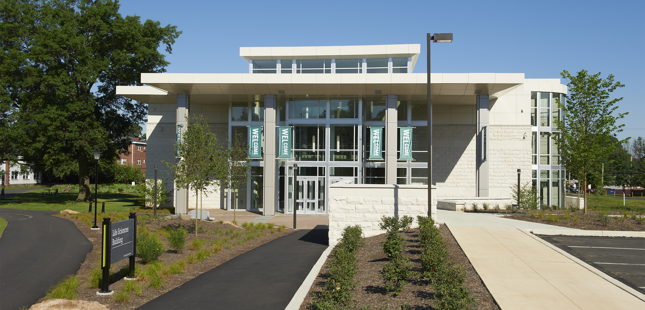 The front of the Delaware Valley College building showcasing the white brick and glass accent design with a front walkway and side parking lot.