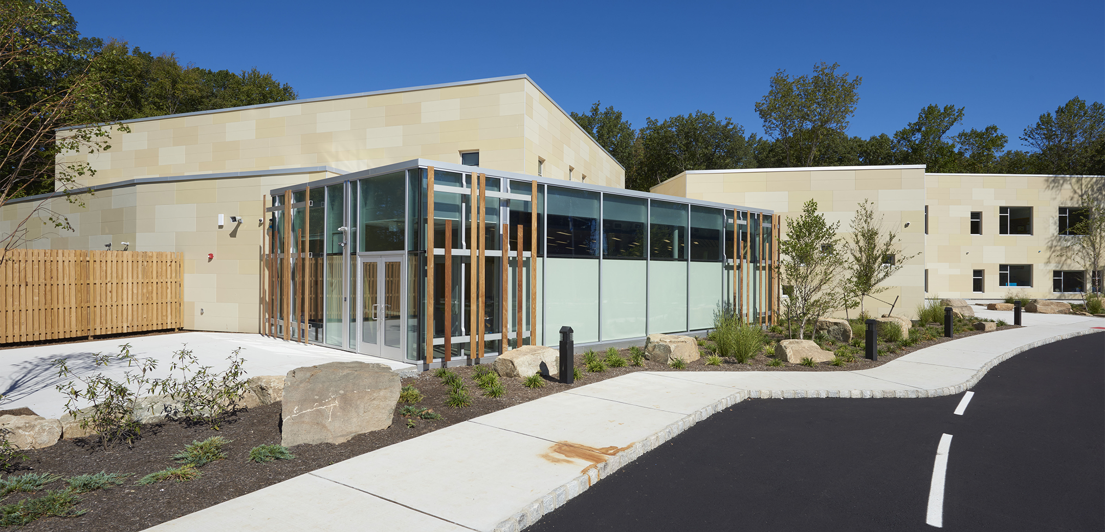 An angled view of the Gottesman RTW Academy back glass exit with a paved courtyard and landscaped area separating the building from the sidewalk.