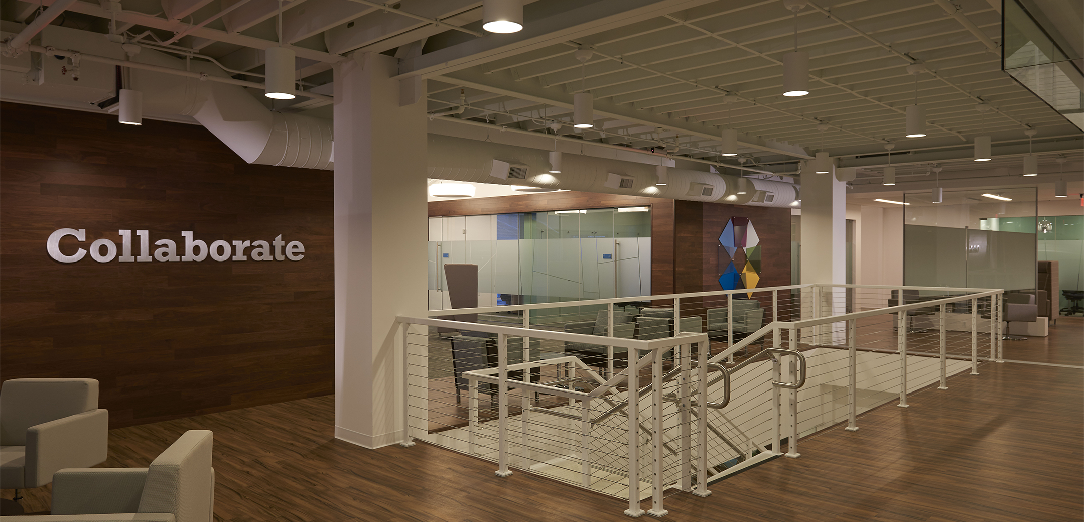 The interior space of Amerisource Bergen featuring a downward staircase in an open lobby space with a Collaborate sign on the wall.