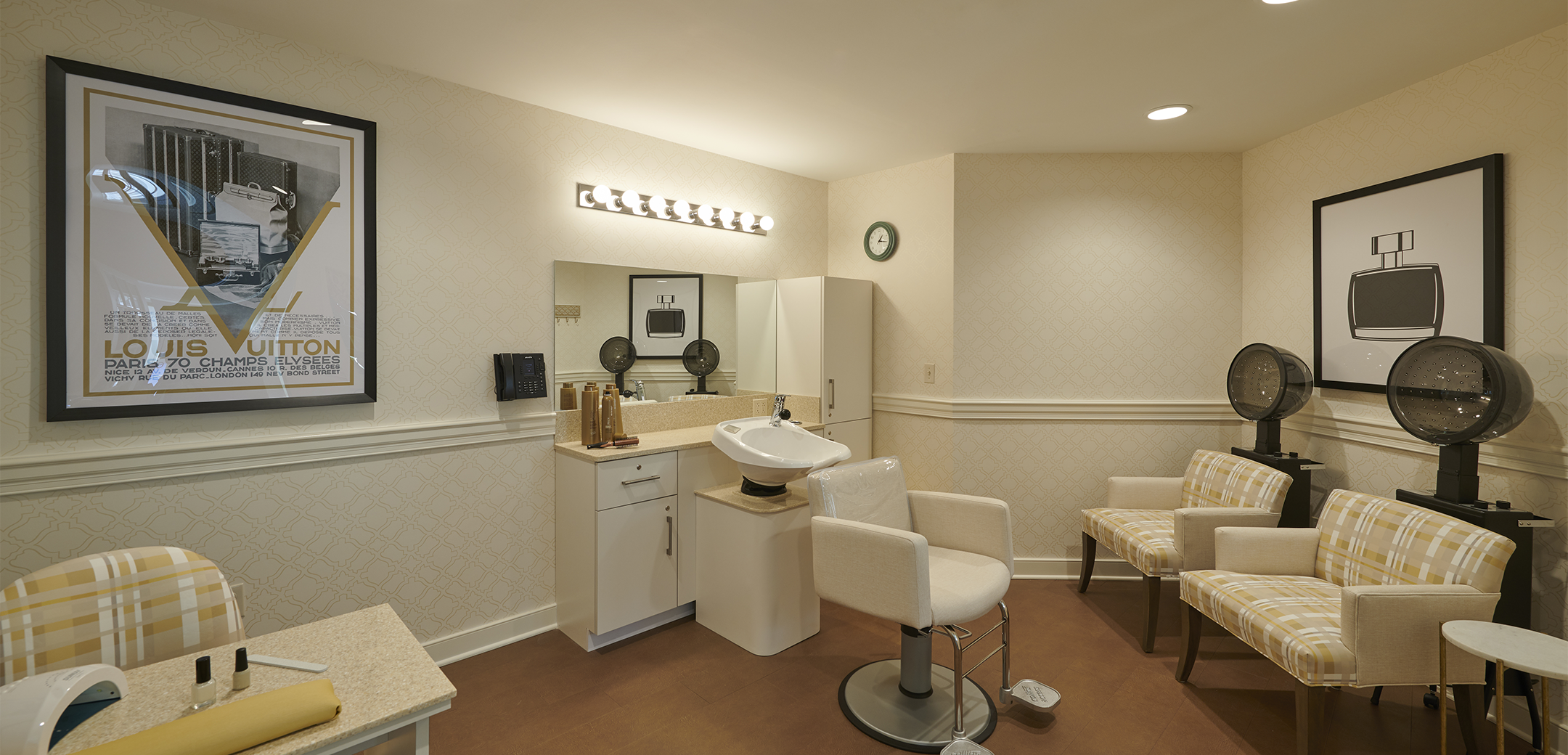 An interior view of the Artis Senior Living spa center with a hair washing station, hair drying seats and manicure table in the foreground.