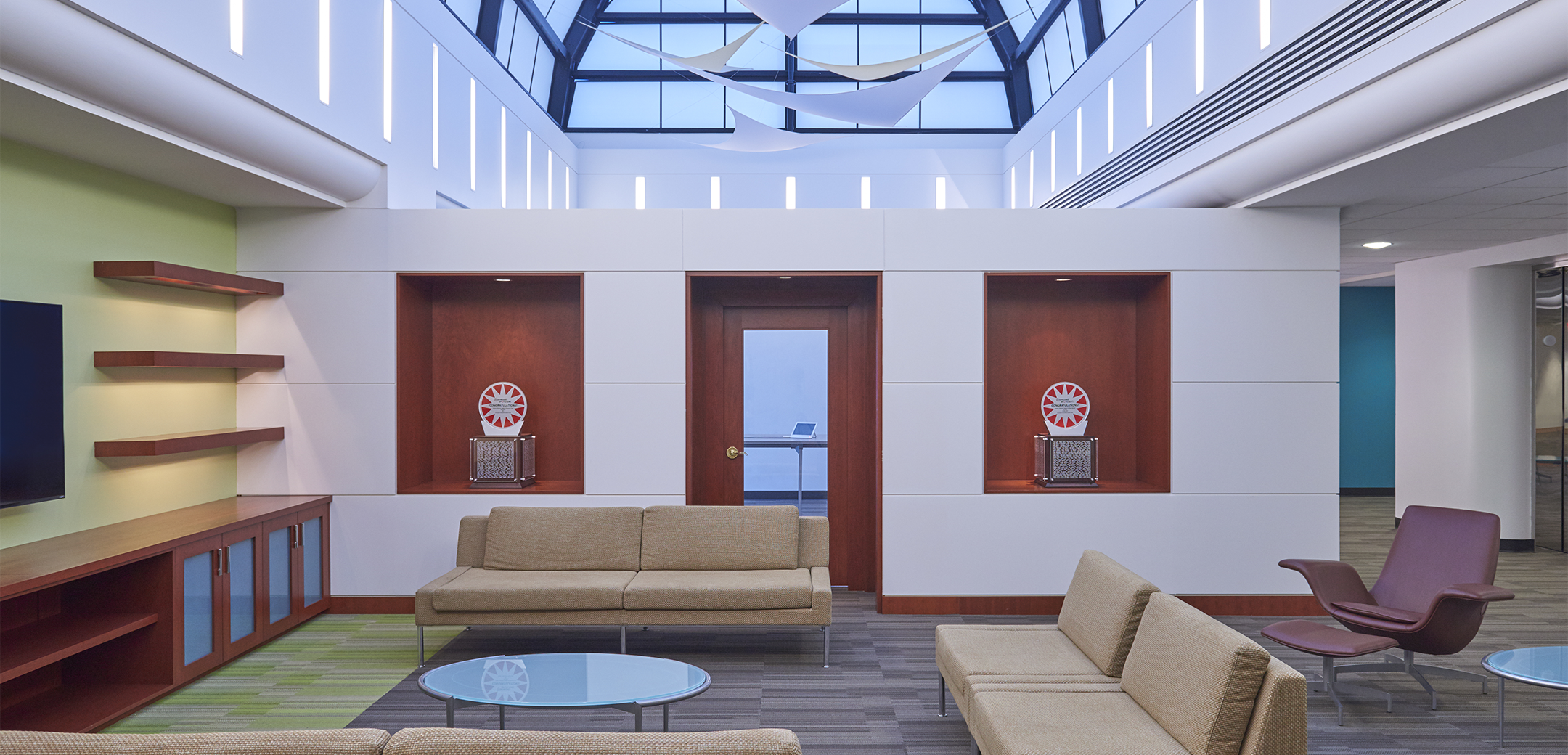 An empty sitting area in Comcast Communications Spotlight with shelving built into the back wall, a conference room, and a glass ceiling ceiling.