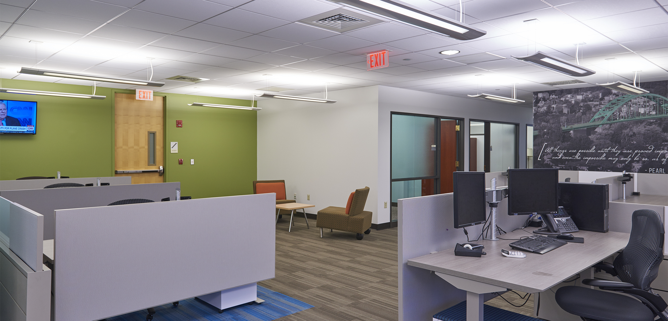 An open office area with several cubicles, a conference room with frosted glass, and a mural with a quote on the back wall.