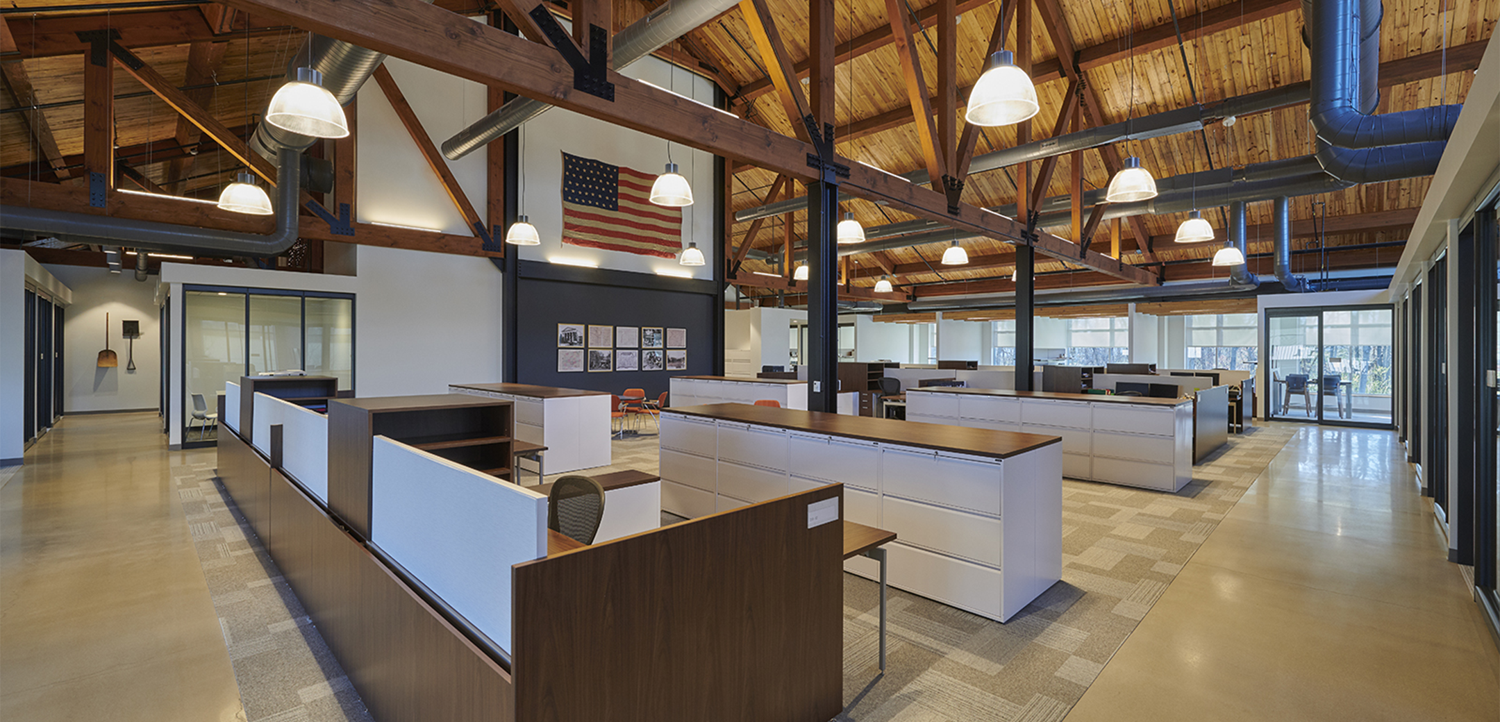 The interior space of Equus Capital Partners headquarters featuring wood ceilings with accent wood trusses, open concept cubicles, and glass paneled conference rooms in the background.