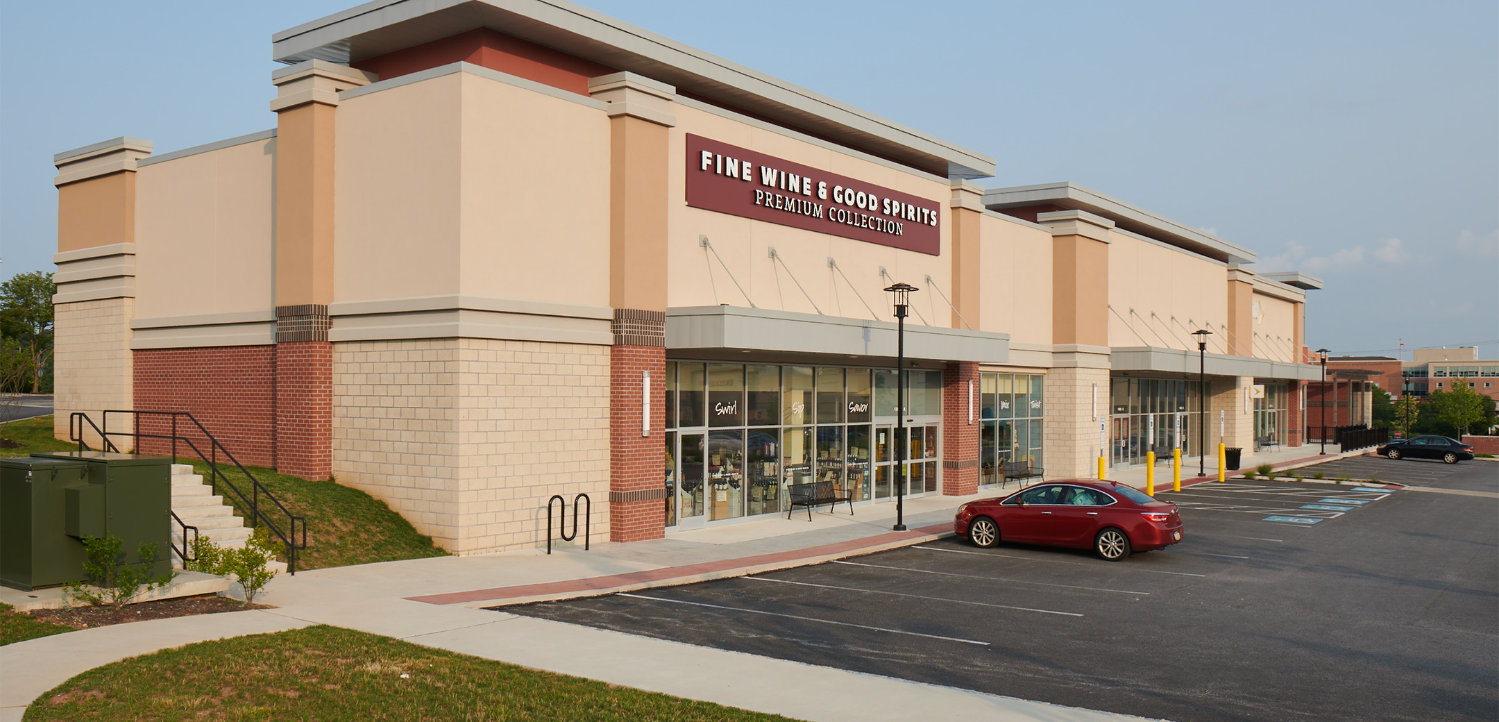An angled view of the Promenade at Granite Run brick building's side showcasing the glass shopfront, "fine wine & good spirits" signage on top and the side parking lot.