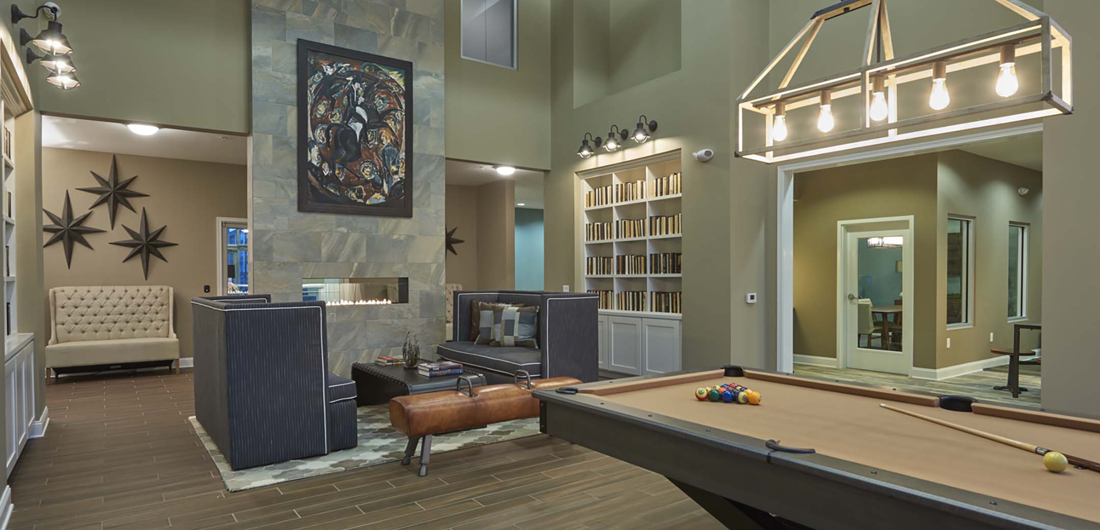 An interior view of the Haven building rest space with couches, bookshelves and a pool table with hanging lights over it.