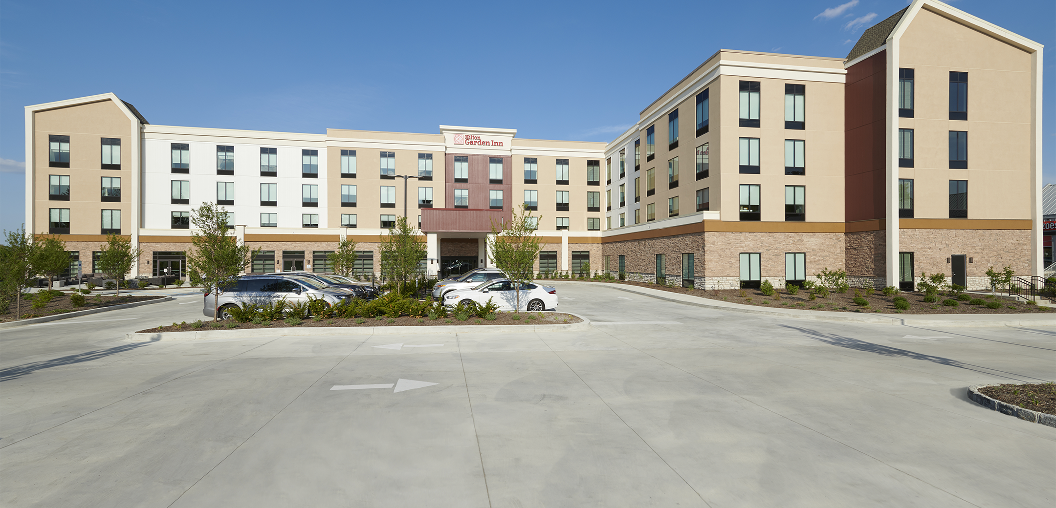 A 4 story Hilton Garden Hotel building showcasing the front side enterance,driveway and parking lot.