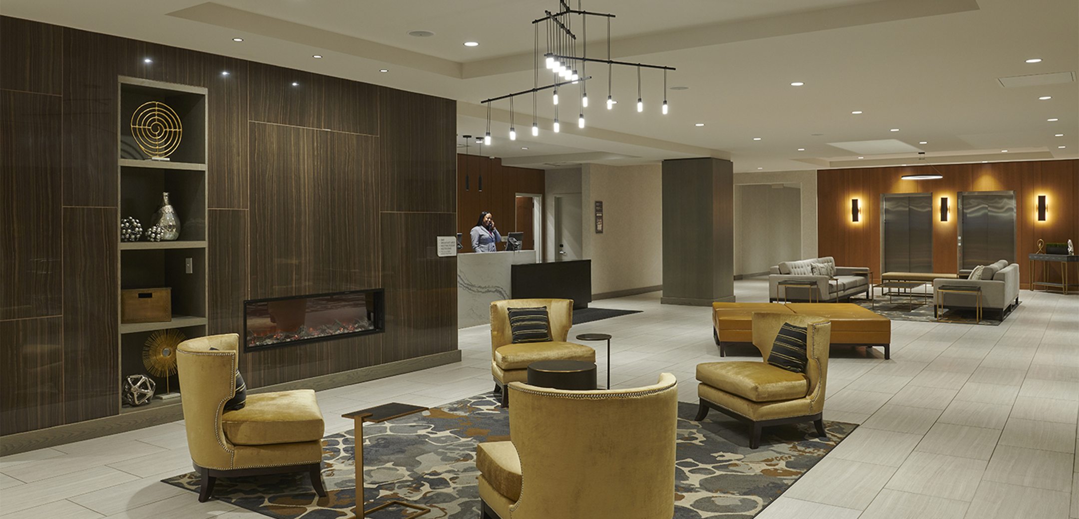 An interior image of the Hilton Garden Hotel foyer and reception lobby showcasing multiple seating areas, one near a fireplace and one near the elevators.