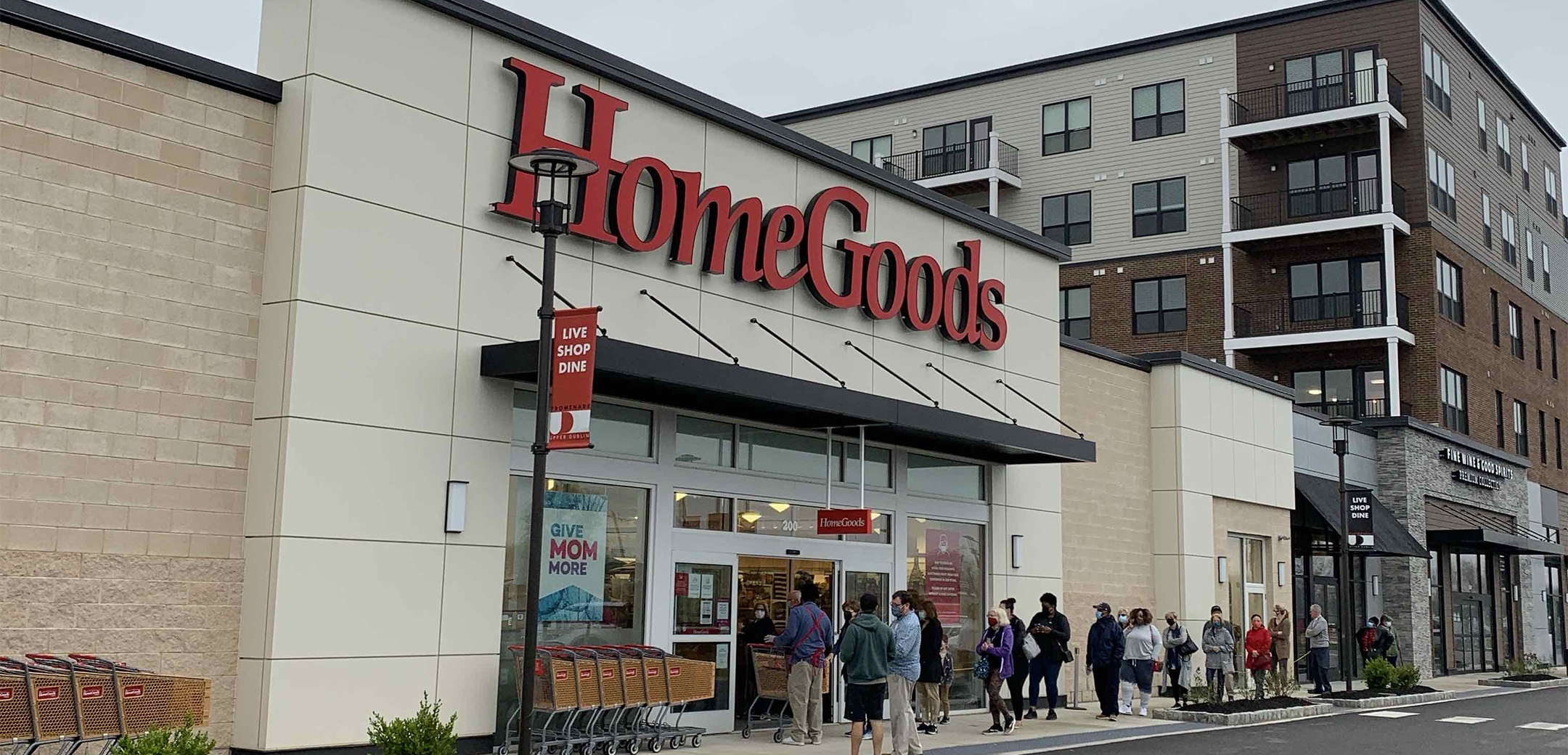 An angled exterior view of the Homegoods building showcasing the street it is on, people going through the front automatic doors and forming a line on the sidewalk.