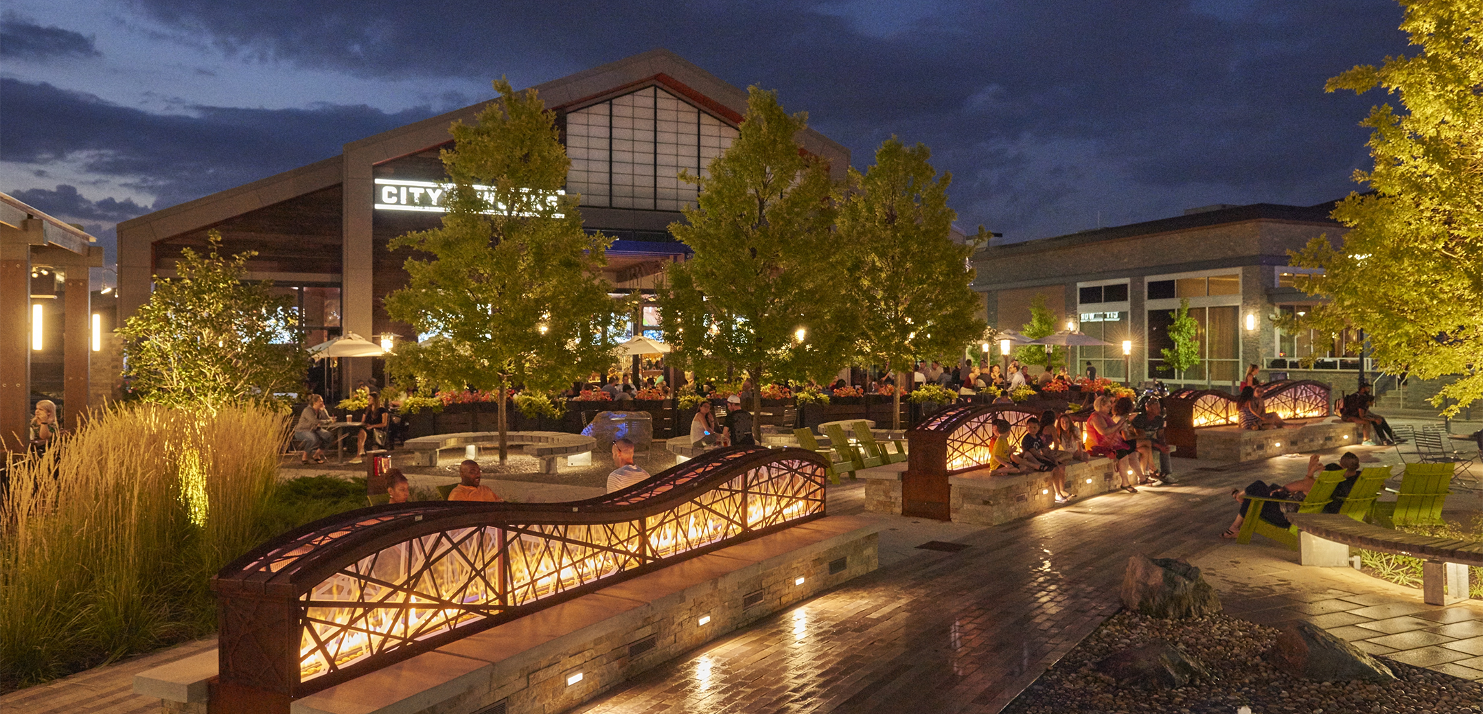 An exterior nighttime view of the KOP Center showcasing the brick seating with lit backrests in the middle of the walkway of the square.