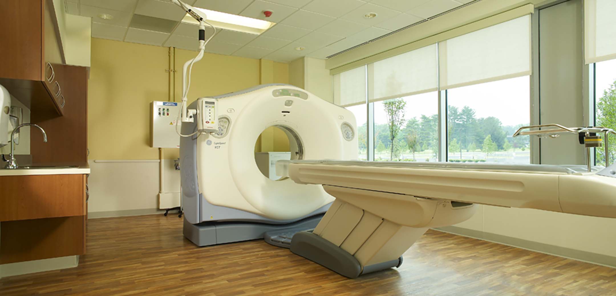 An interior view of the Main Line Health hospital room showcasing the wood flooring and CAT scan machine inside the room.