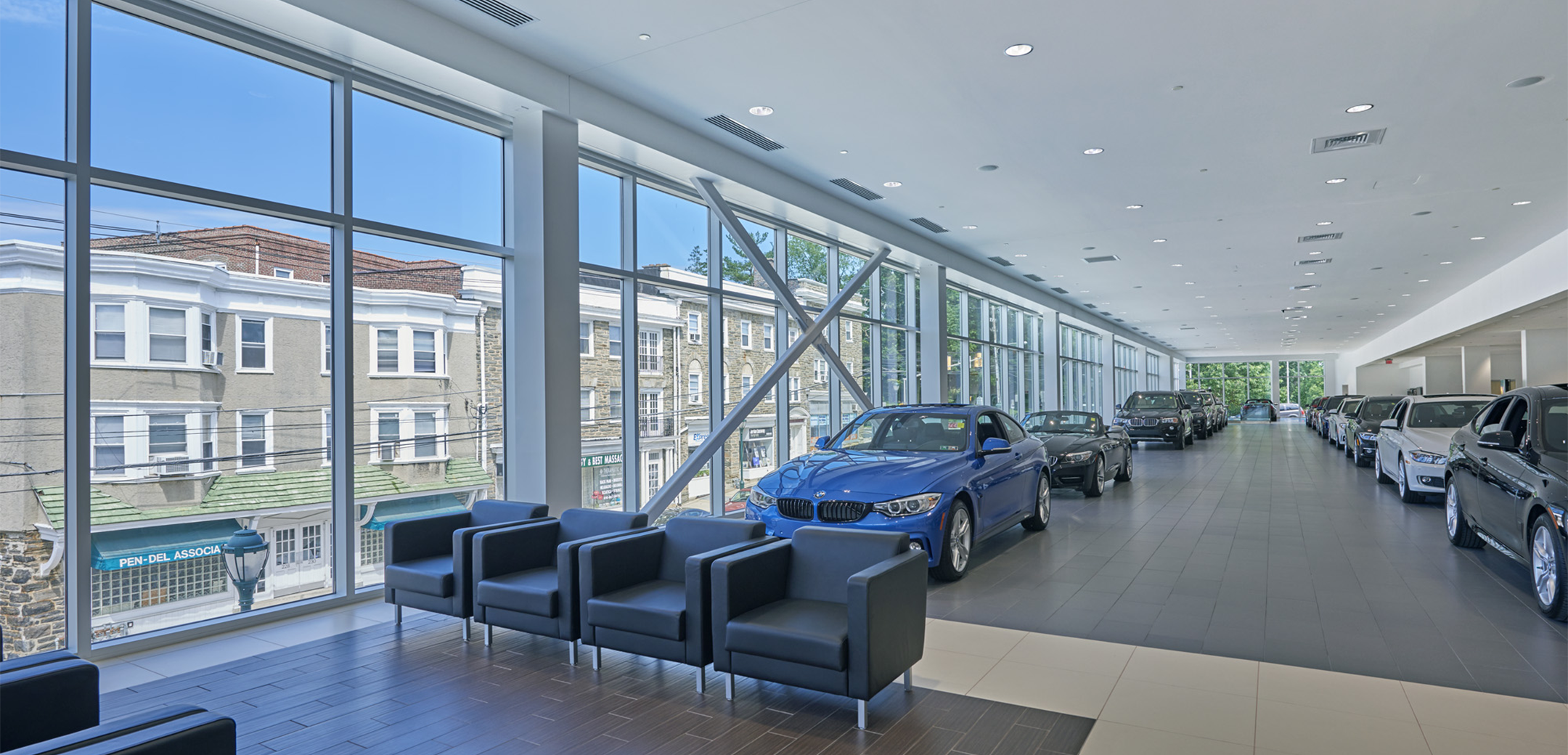 The interior view of the Main Line BMW building's second floor, showcasing the seating area, glass floor to ceiling wall on the left side and cars lined along the walls.