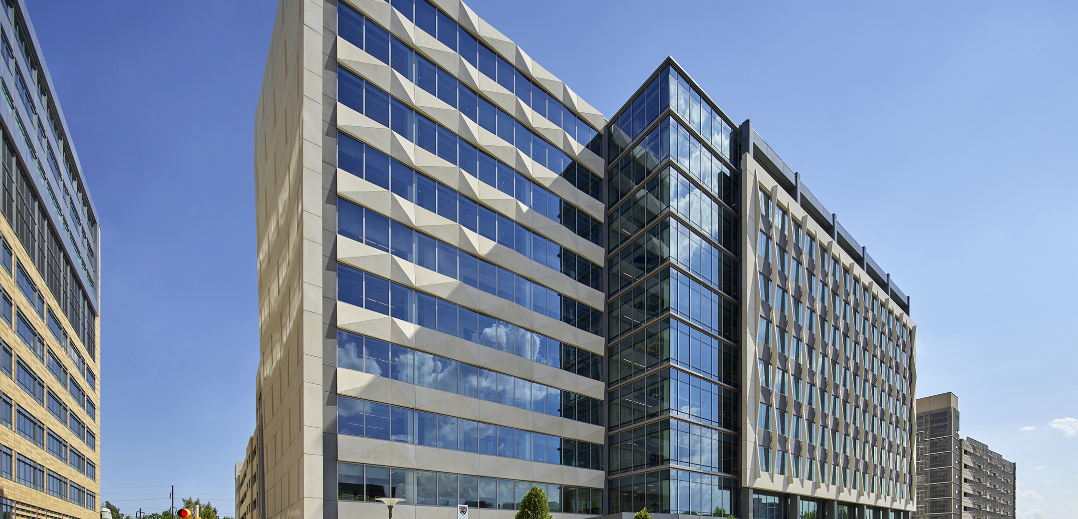 The exterior of a 10-story office tower for Penn Medicine featuring precast panels framing floor-to-ceiling glass on a street lined with trees in Philadelphia.