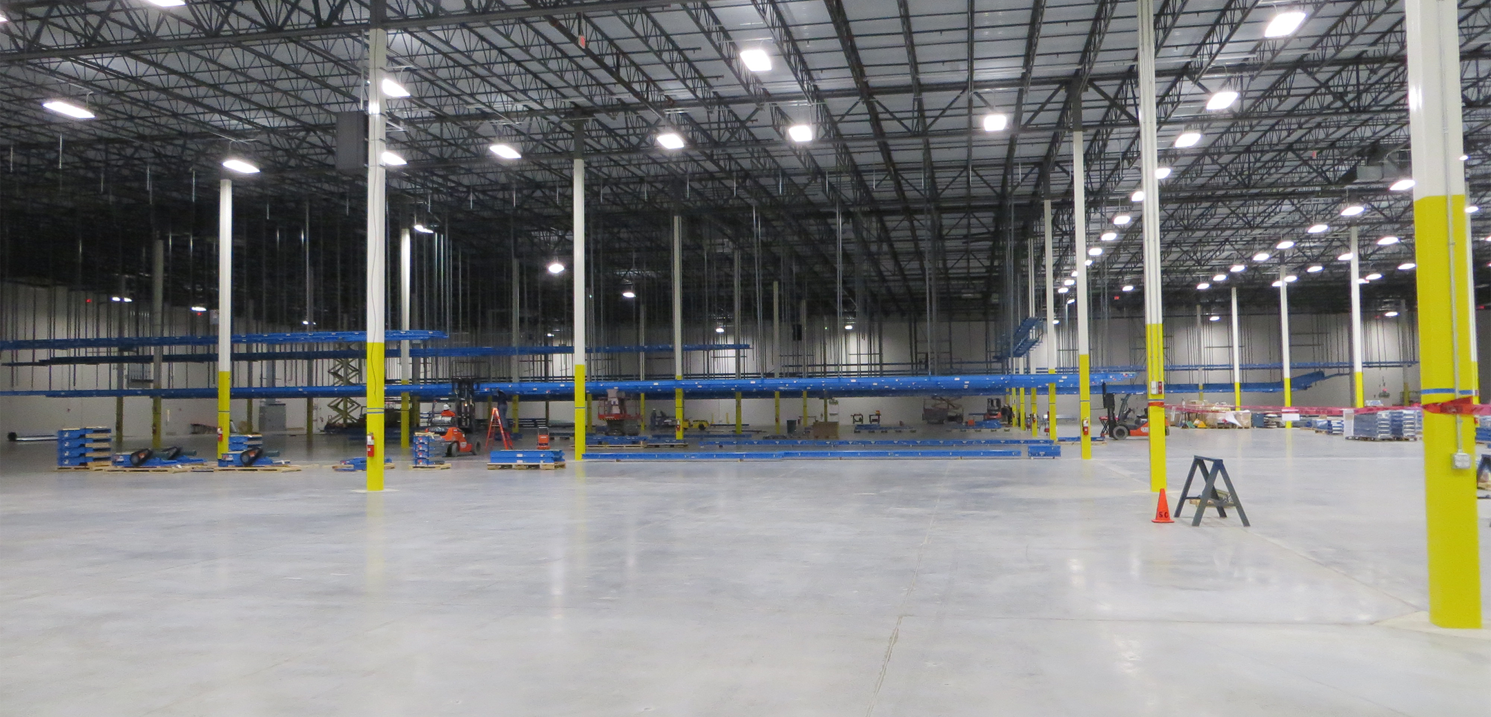 An interior view of the Project Liberty Distribution warehouse with thin support pillars, high industrial ceiling and half constructed shelves in the back.