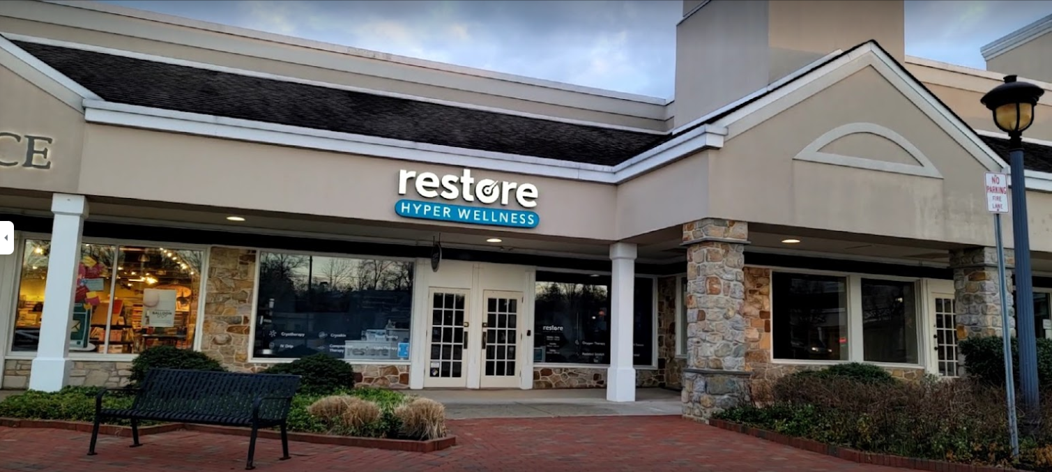 The front of Restore Hyper Wellness building with two white french doors and a light up sign with the company name and logo.