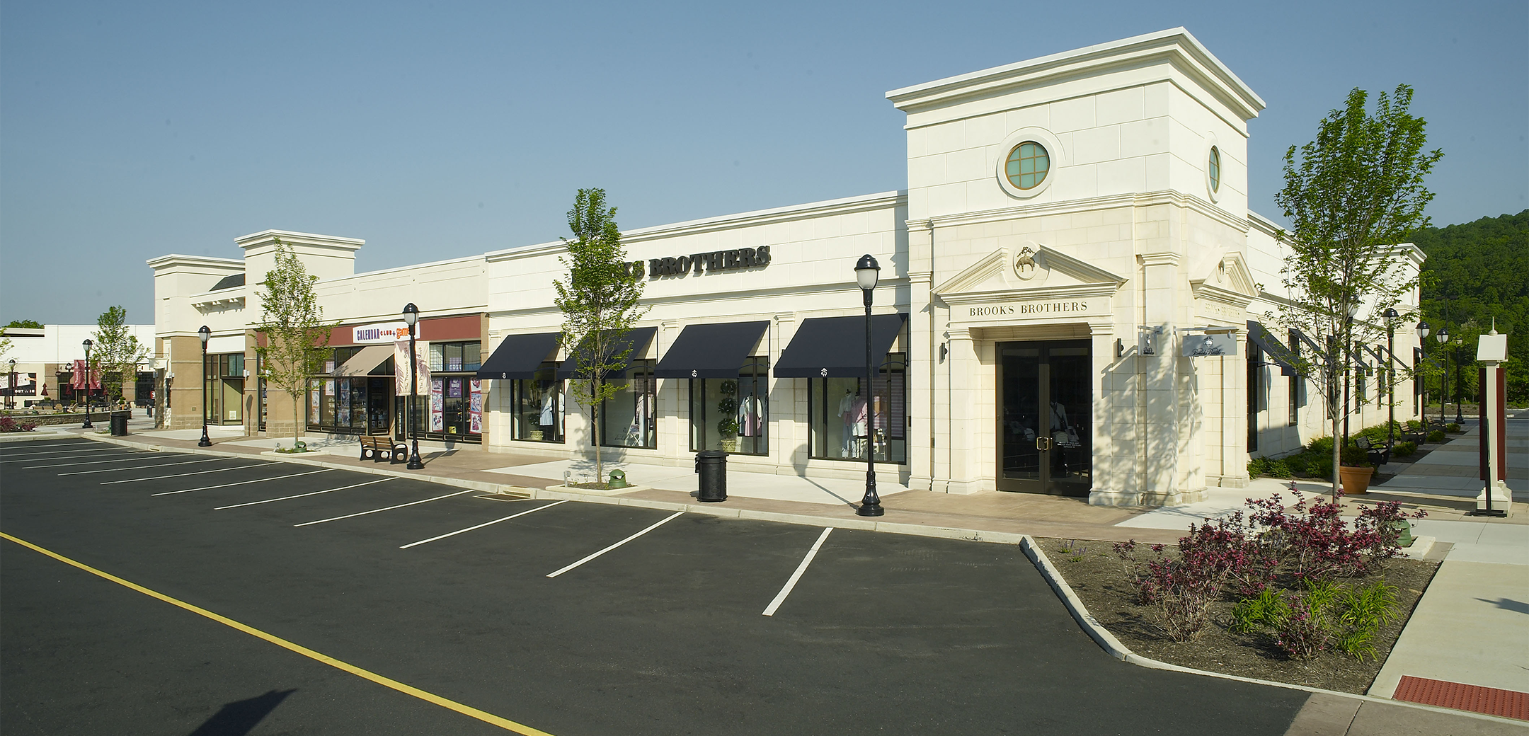 An angled exterior view of the Promenade Saucon Valley building showcasing the storefronts front parking and store logos above the entrances with navy overhangs.