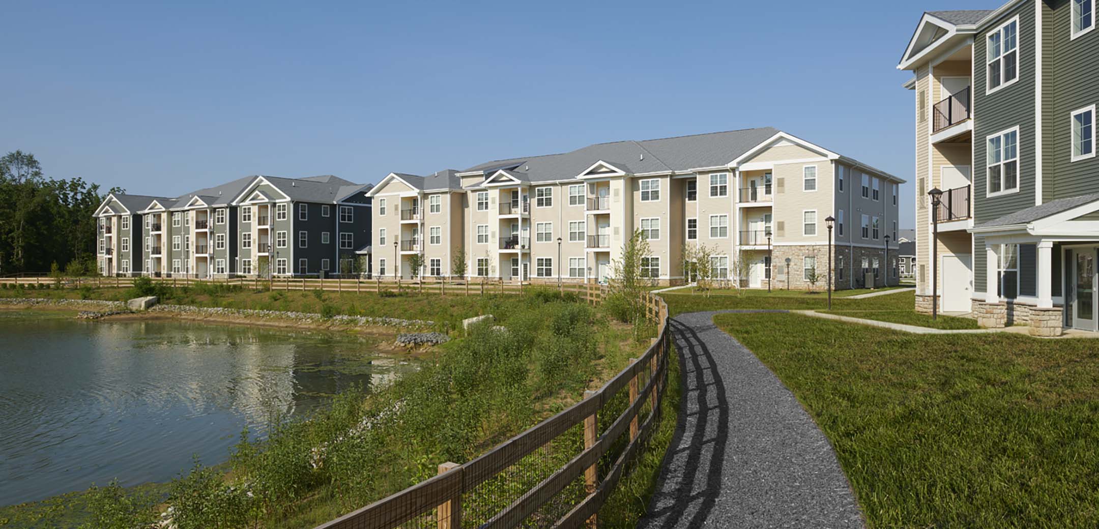 An angled view of the Signature Place MtLaurel apartments showcasing the pond side fenced off path and open grass areas.