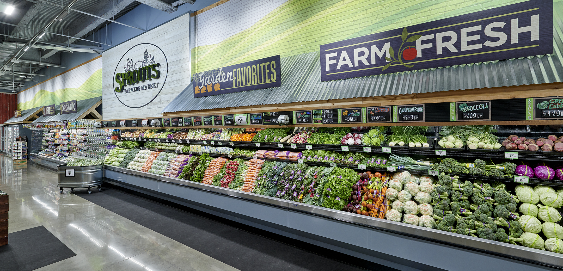A close up view of the Sprouts Farmers Market interior brick decorative wall with "Farm Fresh" signage and vegetables on the refrigerated shelves along the wall.
