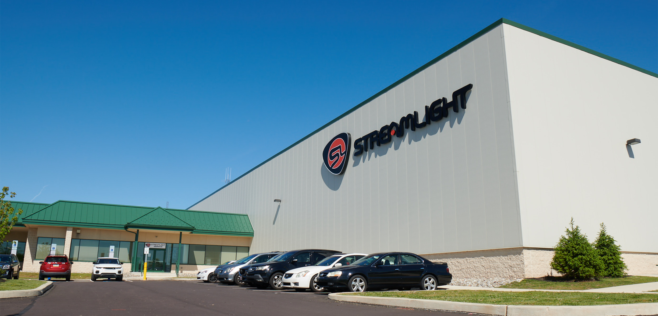 An angled exterior view of the Streamlight warehouse, showcasing the logo, front entrance and parking lot filled with cars.