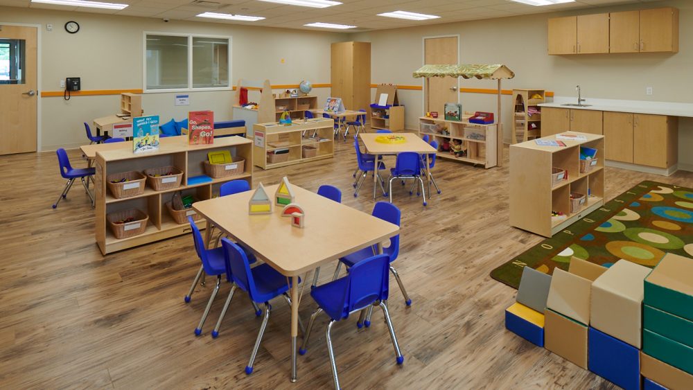 A children's play room with multiple desks, blue chairs, and toys.