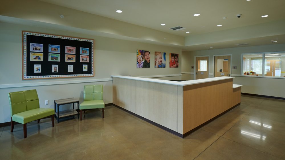 An interior view of the Chesterbrook Academy reception desk with green chairs in a lobby area.