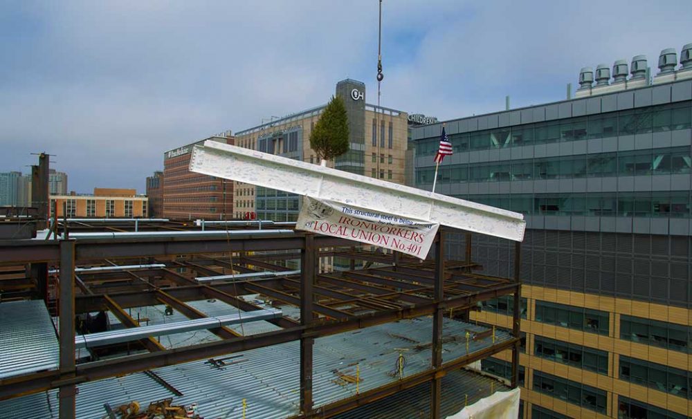 An aerial shot of a white iron beam being hoisted by a crane with a sign that says Ironworkers Local Union