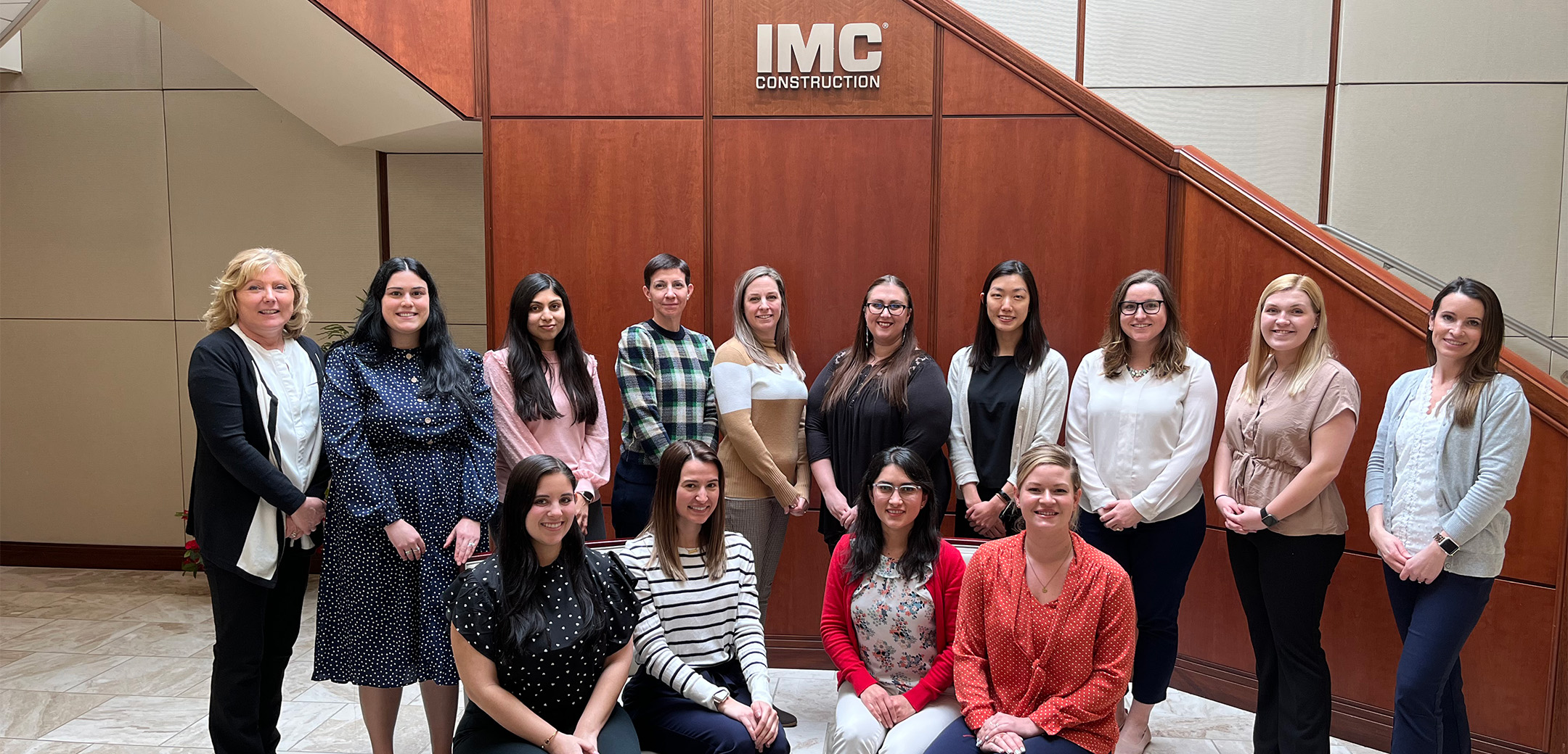 A group of women posing for a group photo in front of the IMC Construction Malvern office lobby