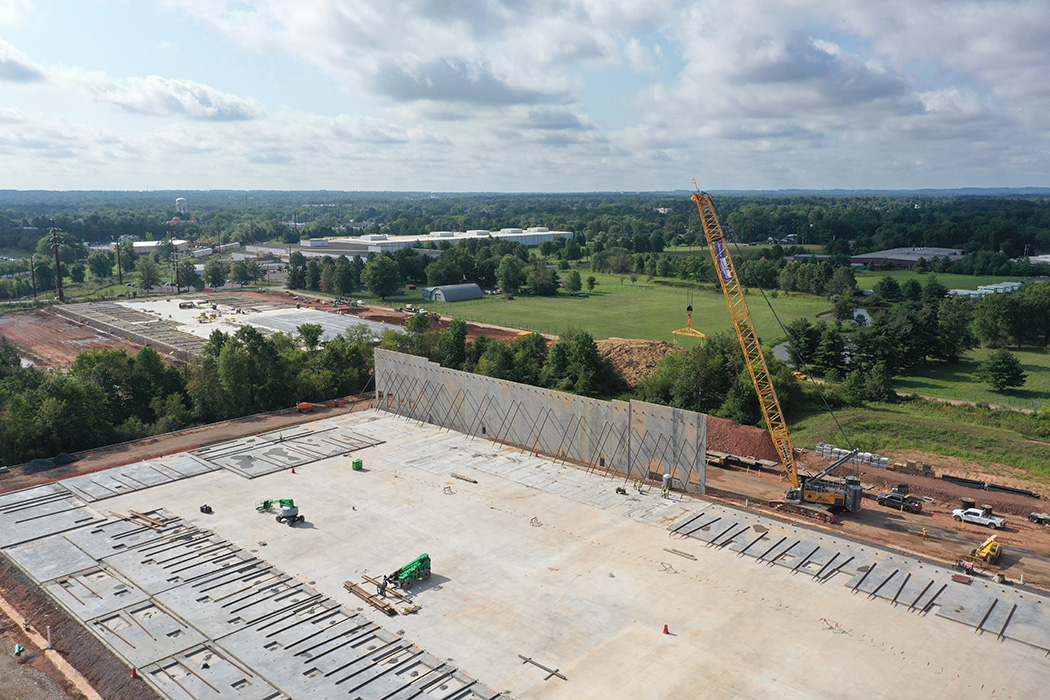An aerial view of a large yellow crane lifting a concrete panel into position on the North Penn Logistics Park project