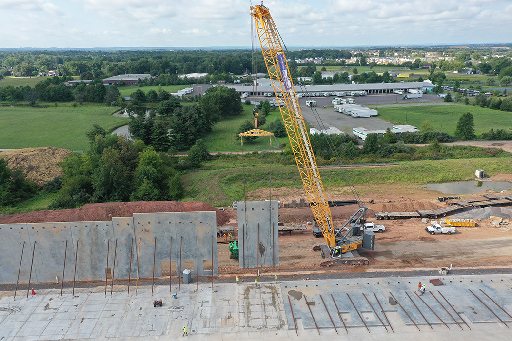 A close up view of a large yellow crane lifting a concrete panel into position on the North Penn Logistics Park project