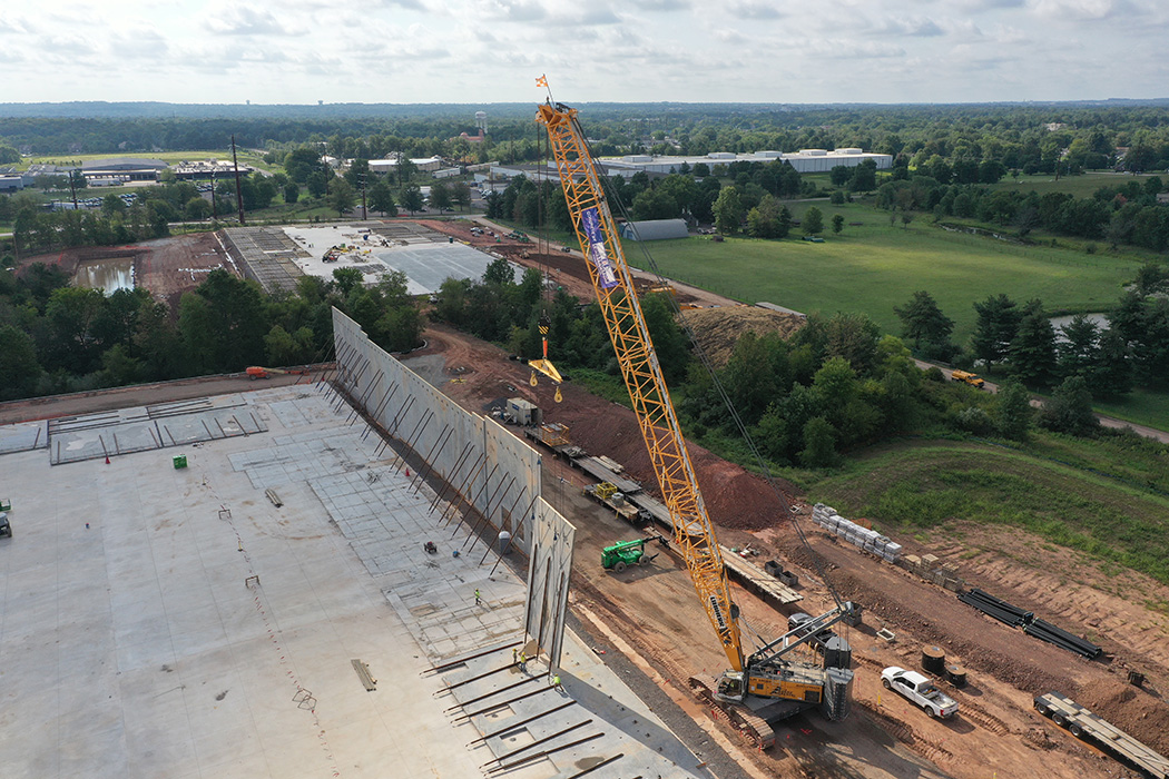 An angled view of a large yellow crane lifting a concrete panel into position on the North Penn Logistics Park project