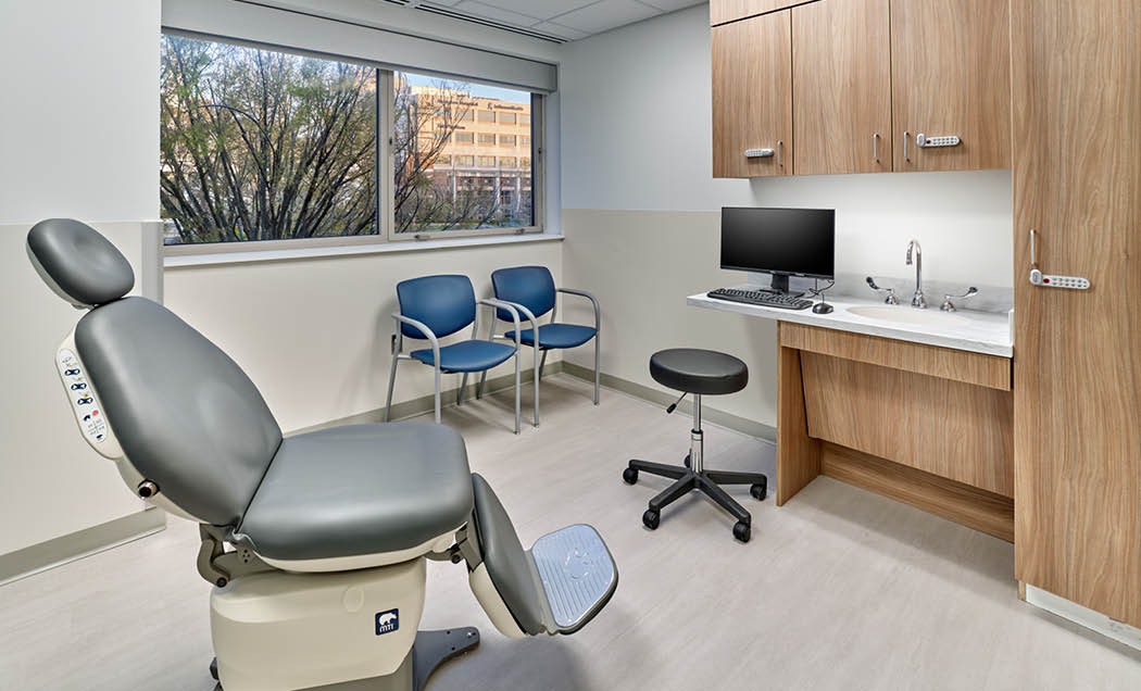 An exam room at ENT and Oral Surgery Suite at Jefferson Health featuring a gray oral surgery chair in the center of the room and a computer screen and wood cabinets